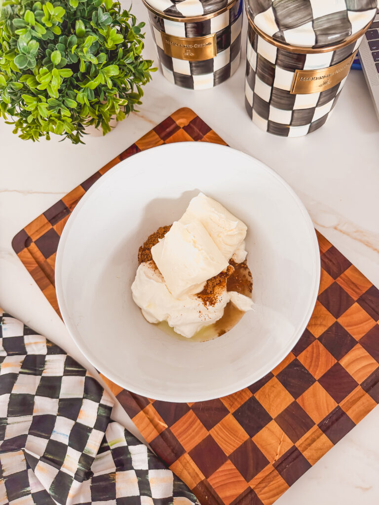 A white bowl with cream cheese, sour cream, and spices on a checkered cutting board.