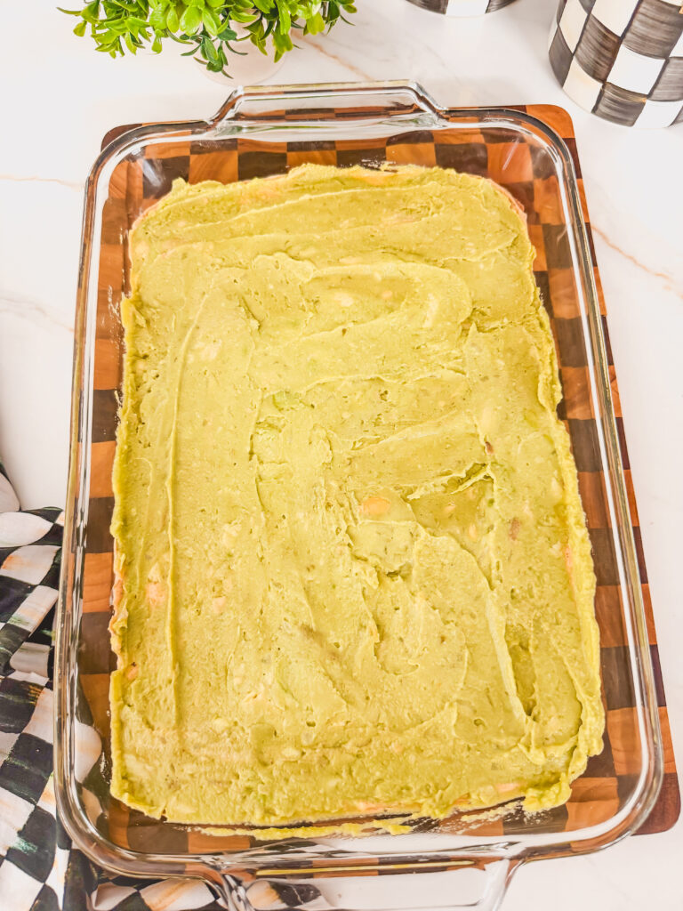 A glass baking dish with refried beans and guacamole layered.