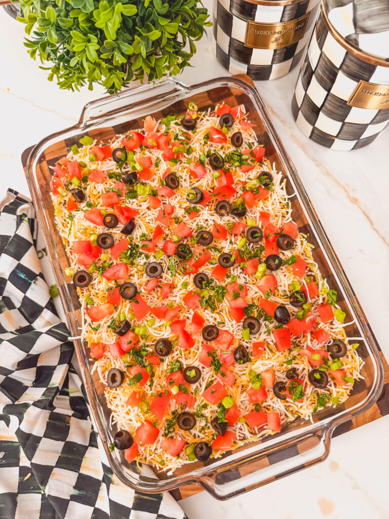 Layered taco dip in a glass baking dish with garnishes. 