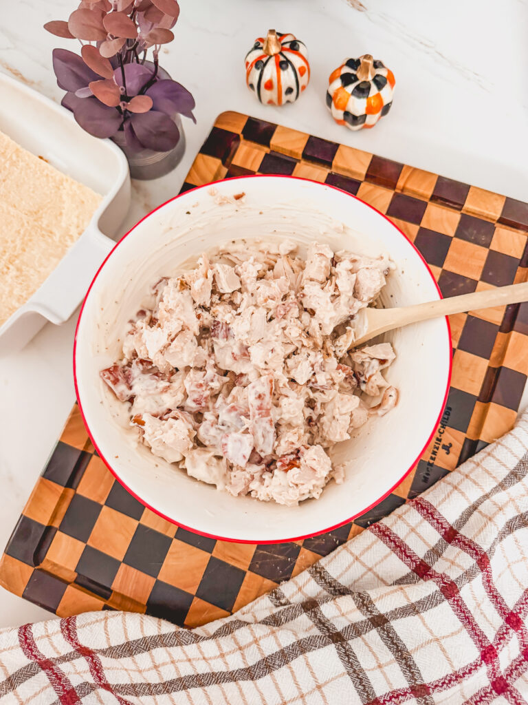 A white bowl with a wooden spoon with chicken, ranch and bacon mixture.