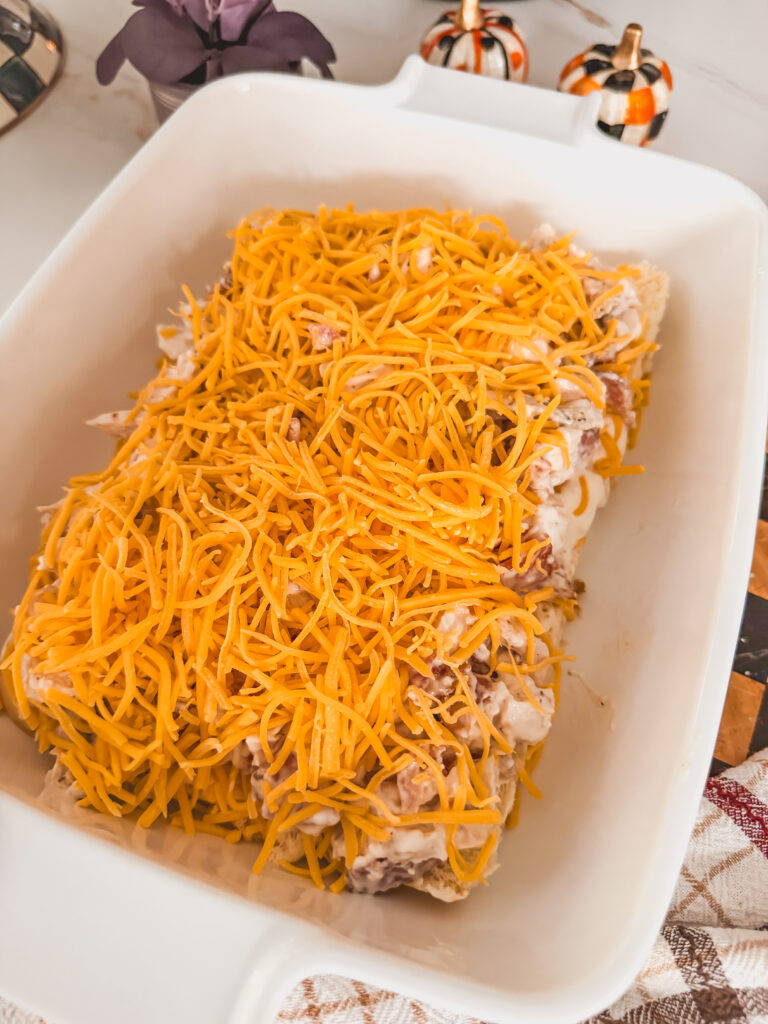 A white baking dish with buns, chicken, ranch and bacon mixture with shredded cheese on top.