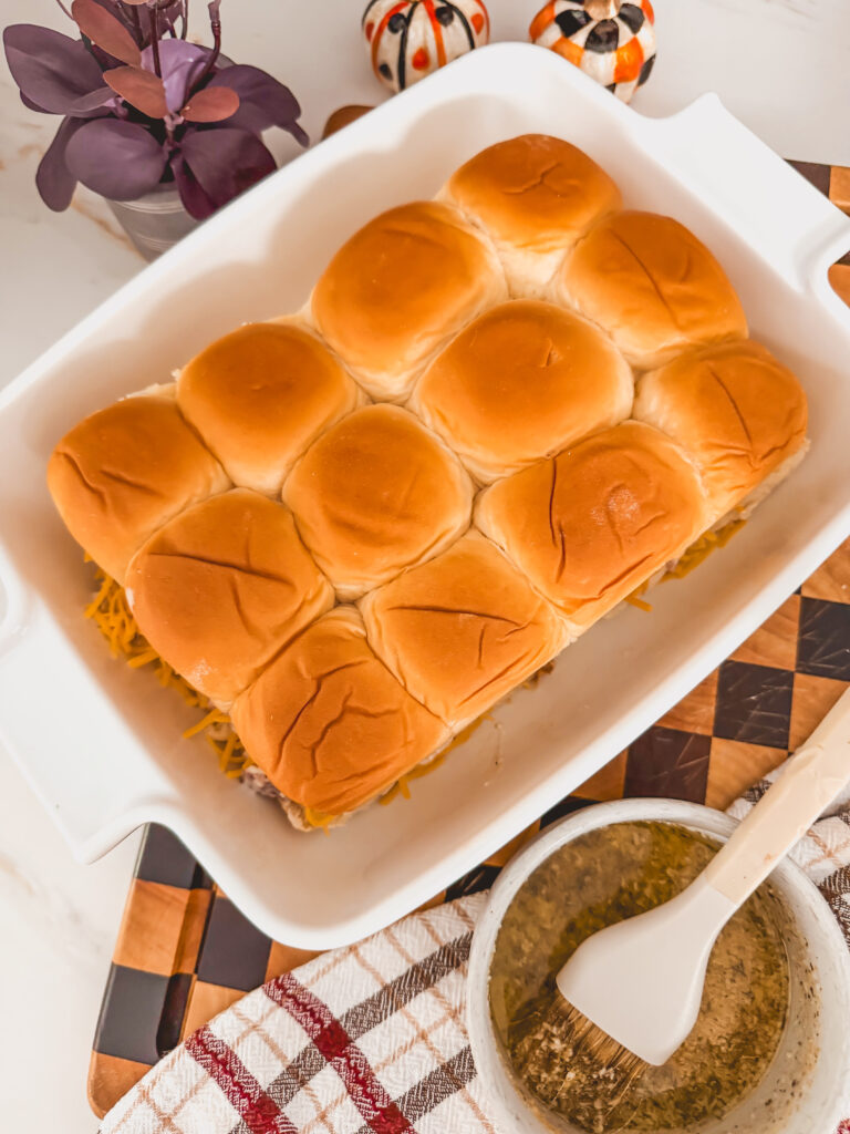 A white baking dish with chicken bacon ranch sliders before baking and seasoned butter on the side.