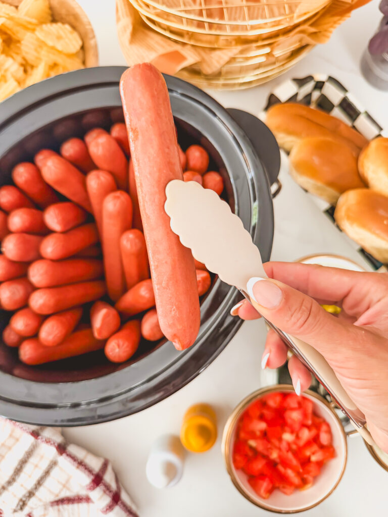 Sow cooker hot dogs being held up with a tong.