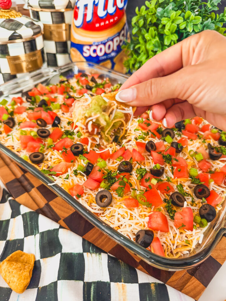 A hand scooping up layered taco dip in a chip.