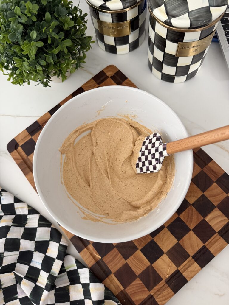 A white bowl with refried beans and a rubber spatula on top of a checkered cutting board.
