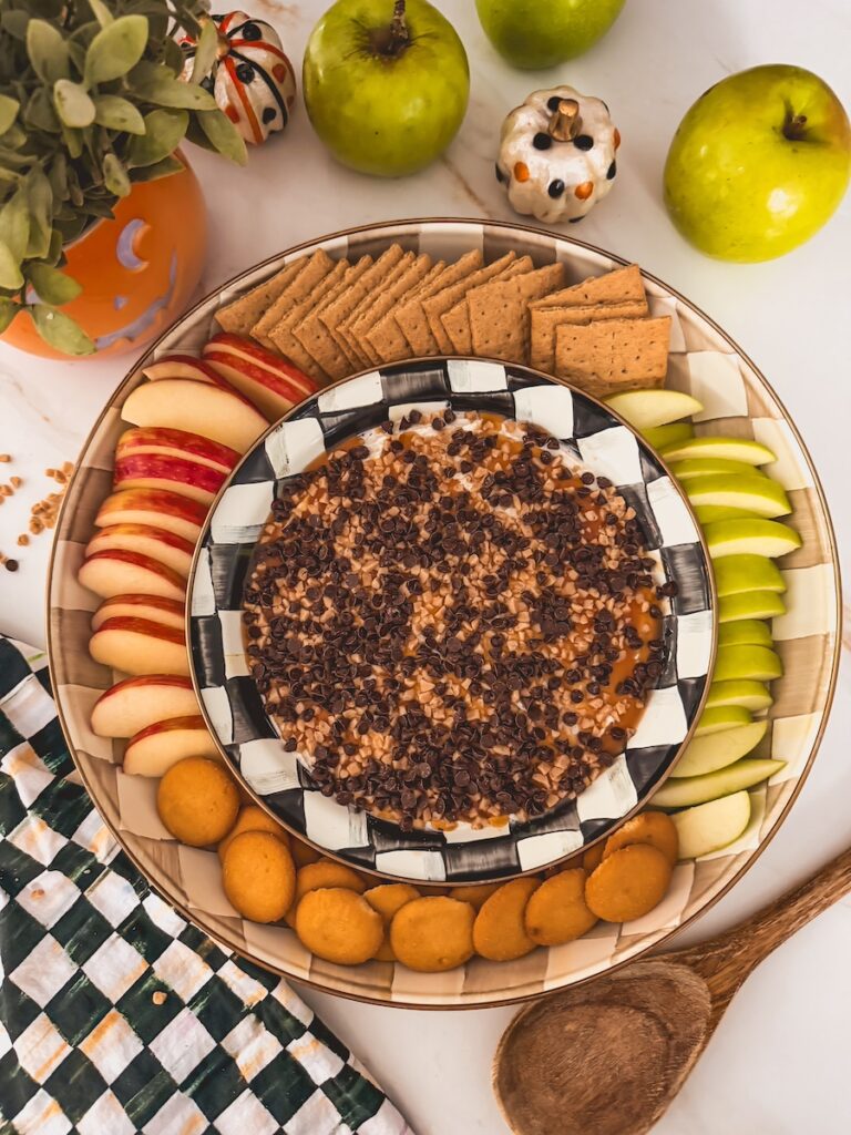 caramel apple cheesecake dip with mini chocolate chips on platter with apples, cookies and graham crackers