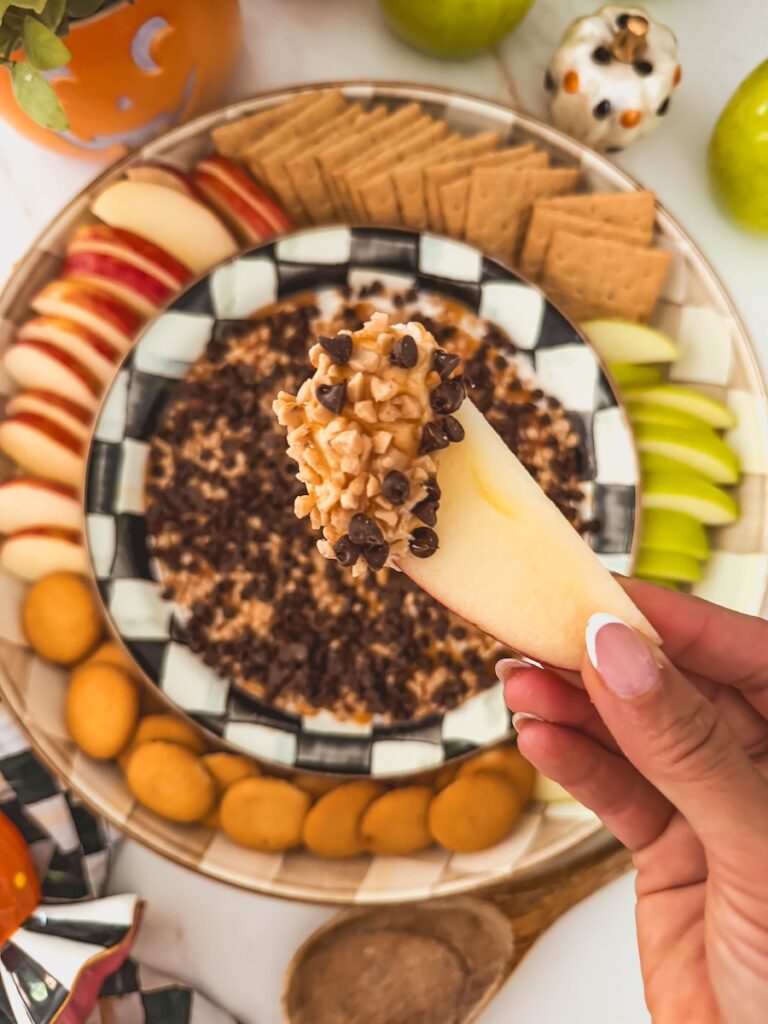 close up with apple slice dipped into caramel apple dip with heath bar pieces, caramel drizzle and chocolate chips