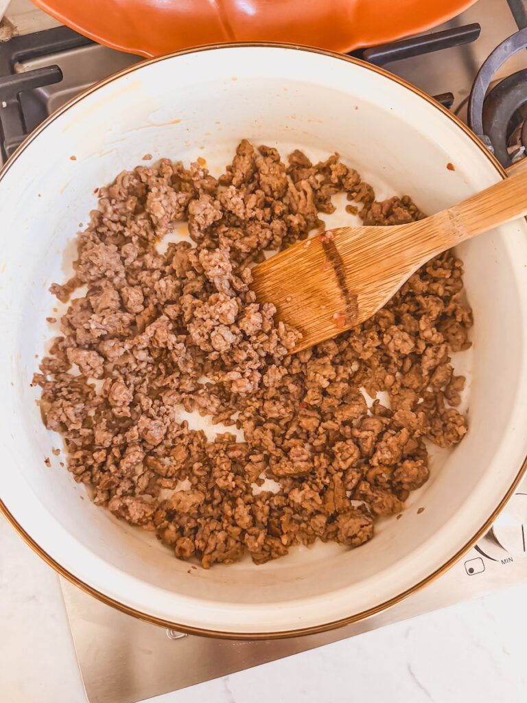 Sausage browning in a skillet with a wooden spoon.