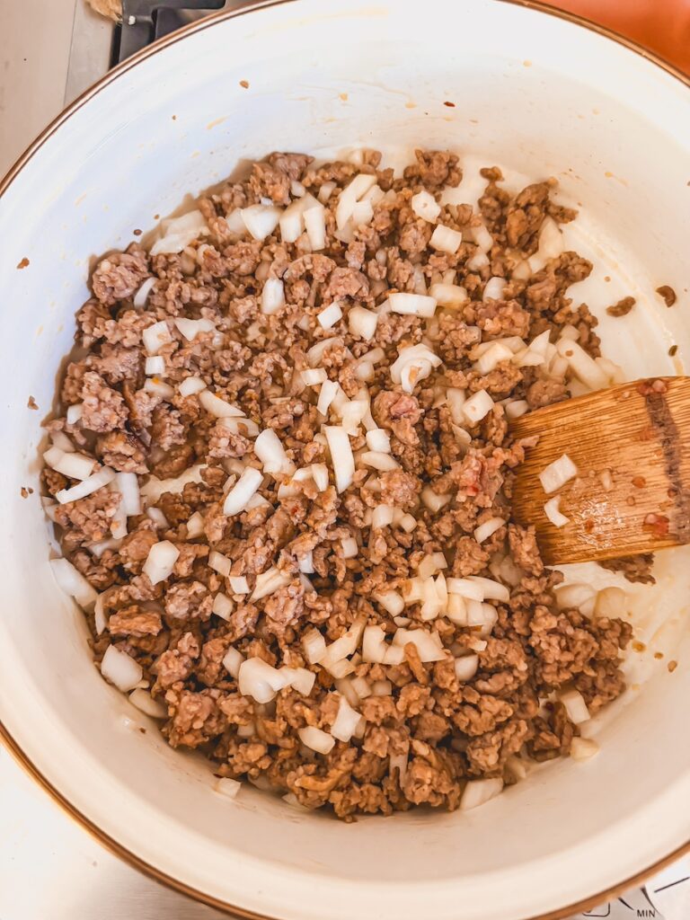 A white skillet with sausage and onions browning.