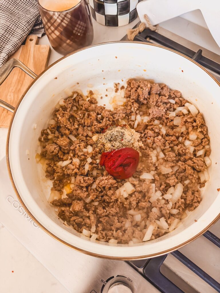 A skillet with sausage, onions, tomato paste, and spices cooking.