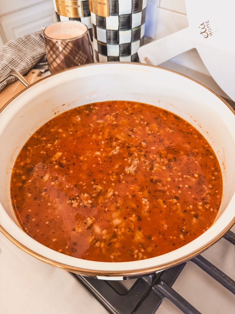 A white pot with ingredients for Italian sausage gnocchi soup coming to a simmer.