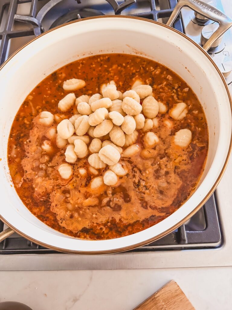 A white pot with ingredients for Italian sausage gnocchi soup with gnocchi on top.