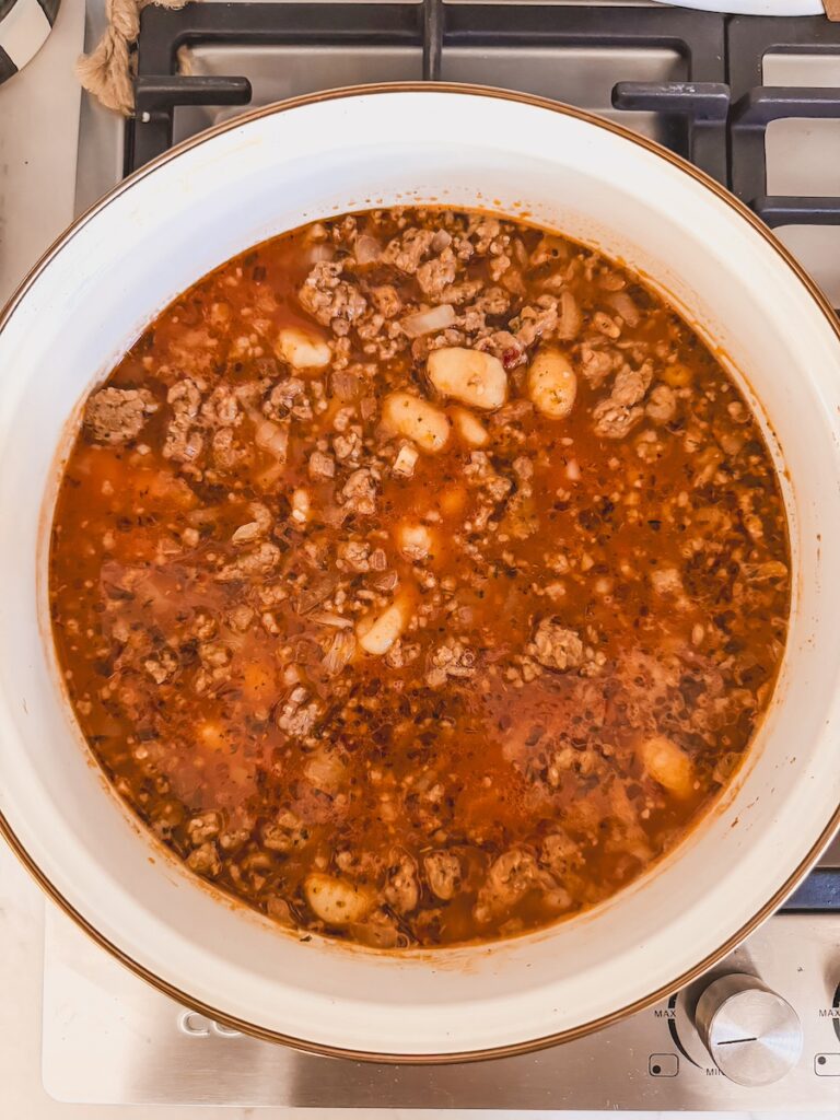 A white pot with ingredients for Italian sausage gnocchi soup.