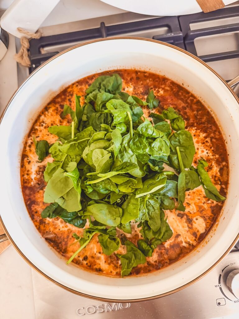 A white pot with ingredients for Italian sausage gnocchi soup with fresh spinach on top.
