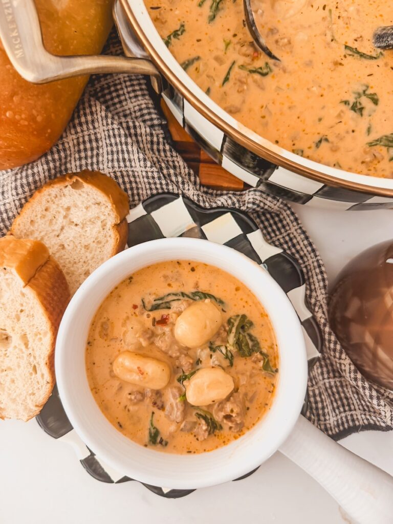 A small white bowl with Italian sausage gnocchi soup and a large pot of soup behind it.