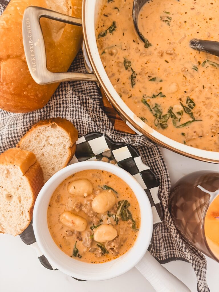 A white bowl with Italian sausage gnocchi soup and a larger pot of soup behind it.