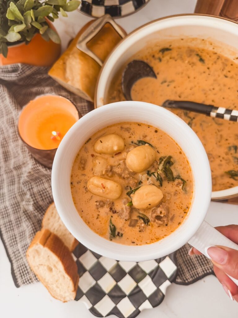 A hand holding a crock of Italian sausage gnocchi soup.