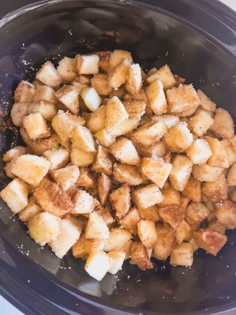 diced uncooked apples mixed with spices and sugar in slow cooker