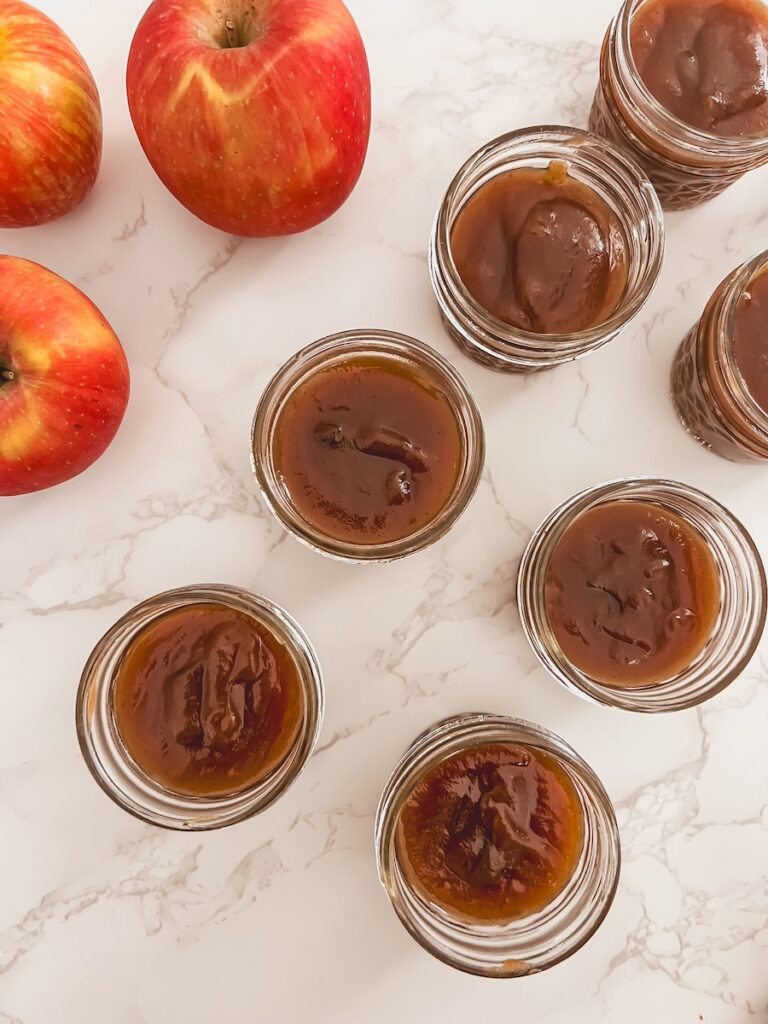 pumpkin apple butter in glass jars next to whole apples