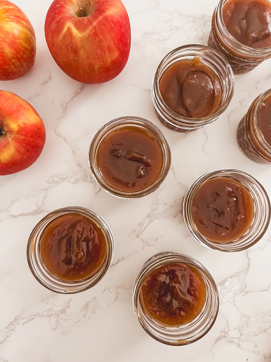 pumpkin apple butter in glass jars next to whole apples