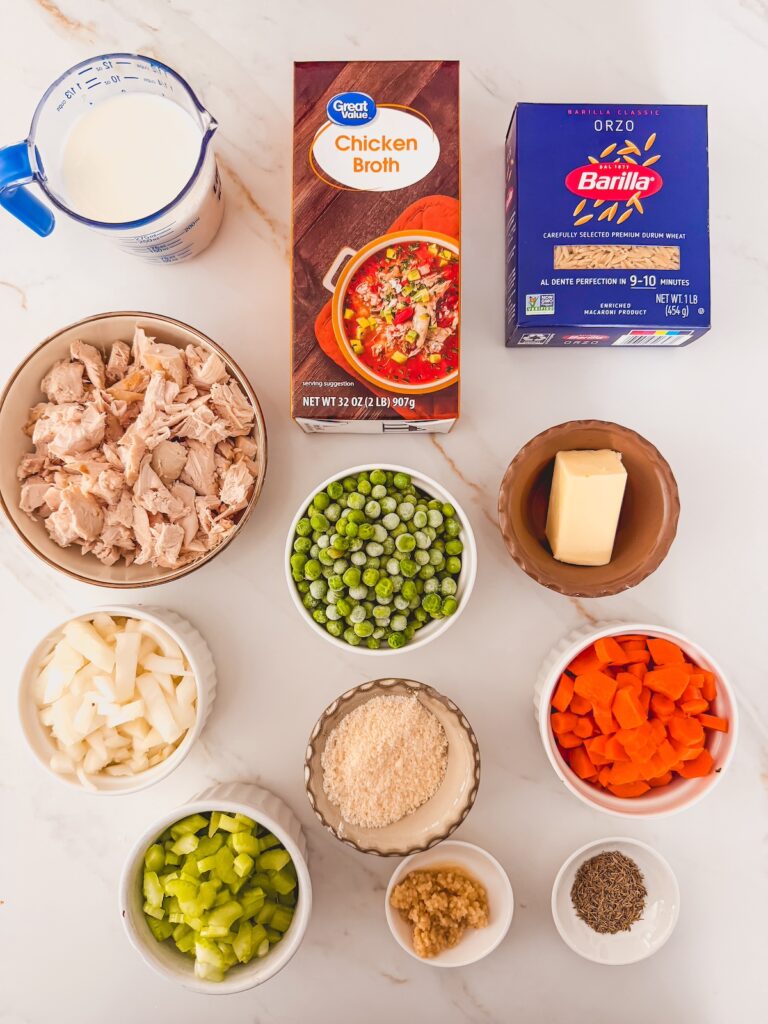 flatlay of ingredients for chicken pot pie orzo including orzo, chicken broth, rotisserie chicken, Parmesan cheese, peas, carrots, celery, butter, thyme, garlic, milk