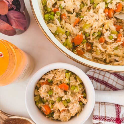 chicken pot pie orzo in a white bowl next to serving bowl with carrots , celery and peas