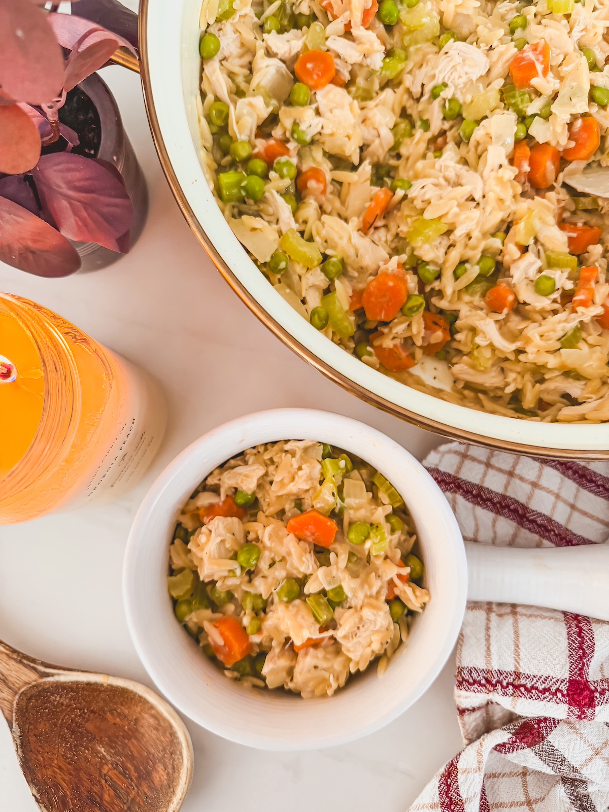chicken pot pie orzo in a white bowl next to serving bowl with carrots , celery and peas