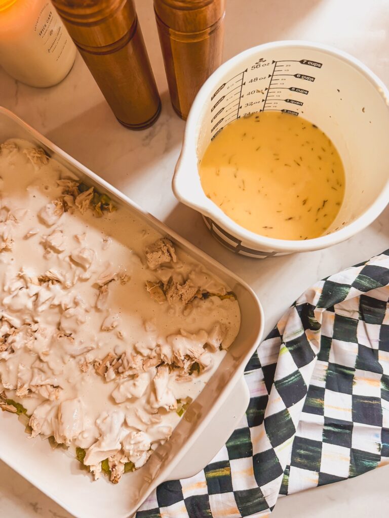 chicken and sauce in baking dish with cream of mushroom soup mixture in white measuring cup next to it