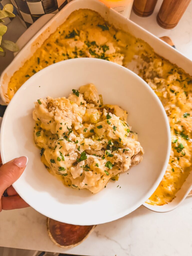 chicken and dumpling casserole in white bowl, held by hand. casserole dish in background.