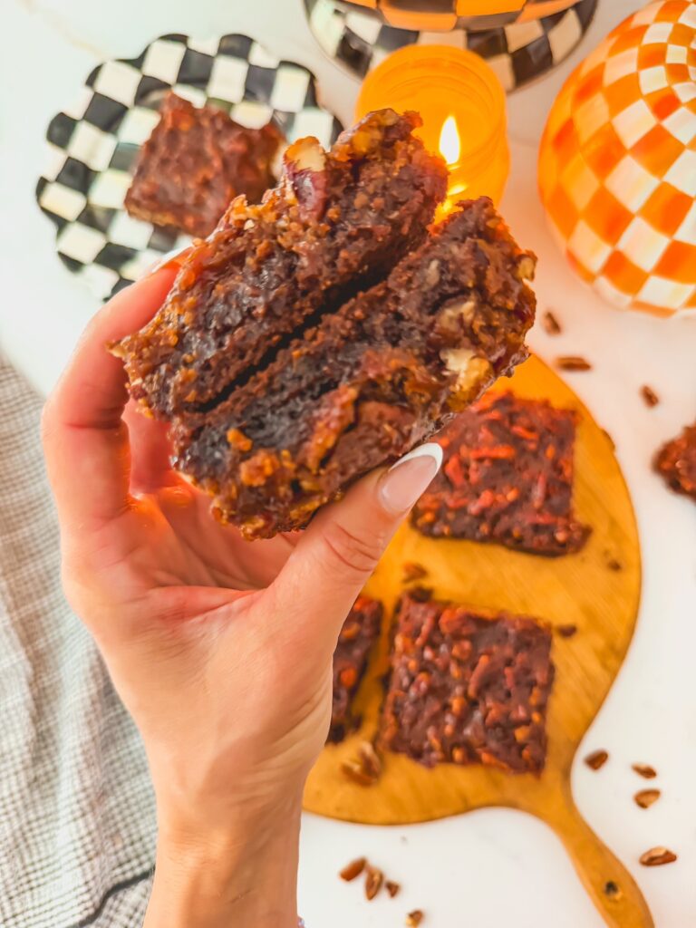 hand holding two brownies with brownies on a board underneath. checkered black and white and orange and white plates in background with candle.