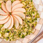 shaved brussels sprouts salad with fanned apple on top, on checked plate