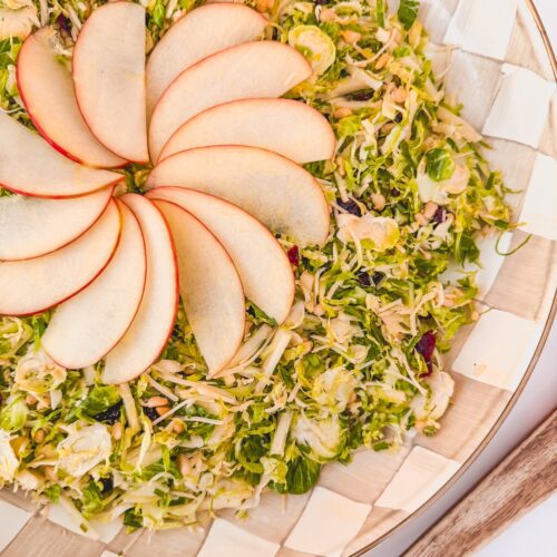 shaved brussels sprouts salad with fanned apple on top, on checked plate